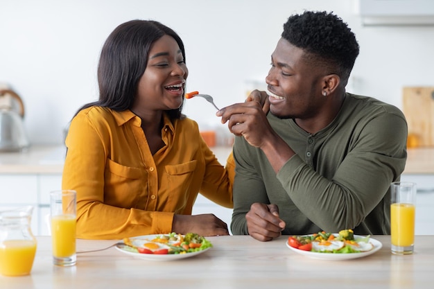 Felizes jovens cônjuges negros desfrutando de seu café da manhã em casa juntos