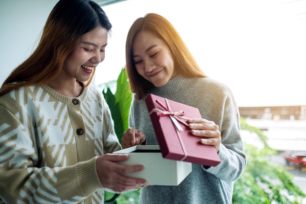 Felizes jovens mulheres asiáticas abrindo uma caixa de presente juntos