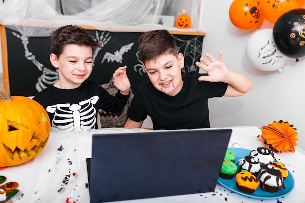 Felizes meninos, irmãos conversando com os avós através de videochamada usando o laptop no dia de halloween, meninos animados em fantasias, olhando para o computador acenando e sorrindo.