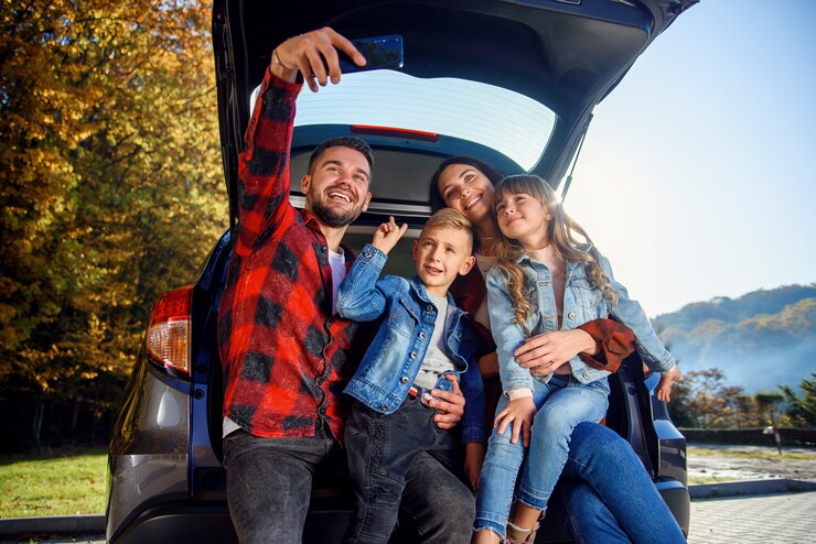 Felizes pais elegantes com seus filhos adoráveis fofos estão fazendo selfie engraçada telefone inteligente enquanto está sentado no porta-malas. Feliz e moderno conceito de família.