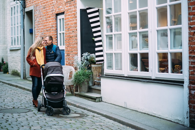 Felizes pais jovens com carrinho de bebê na rua de lubeck (alemanha)