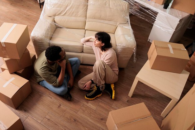 Felizes parceiros casados relaxando no chão da casa depois de comprar o apartamento junto com o empréstimo hipotecário para se mudar. Vista superior de.