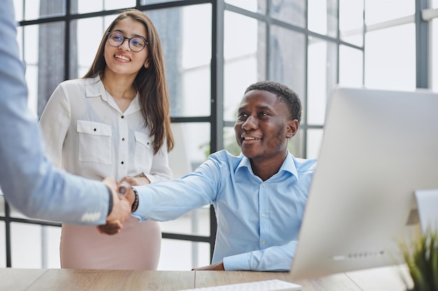 Felizes parceiros do Oriente Médio e afro-americanos usando laptop na área de trabalho da mesa