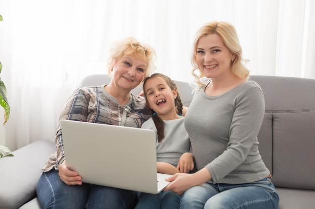 Felizes três gerações de mulheres sentadas, relaxadas no sofá, rindo, assistindo a um vídeo engraçado no laptop, sorrindo, fêmeas positivas, avó, mãe e filha se divertindo, descansando no sofá, curtindo um filme no computador