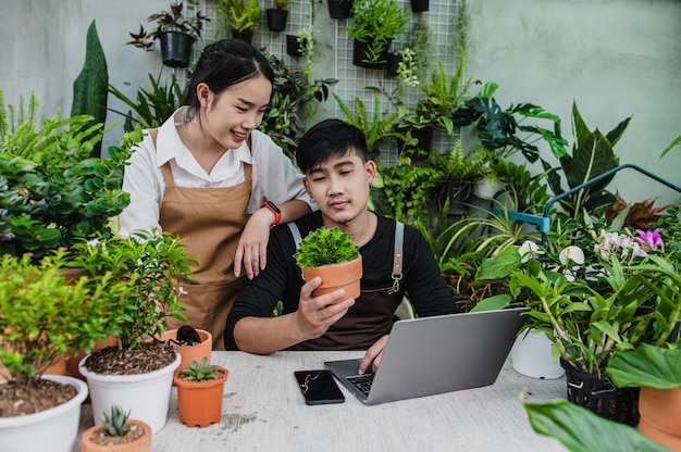 Felizmente, um casal de jardineiros usa um laptop enquanto faz um tutorial online sobre plantas em vasos em uma oficina.