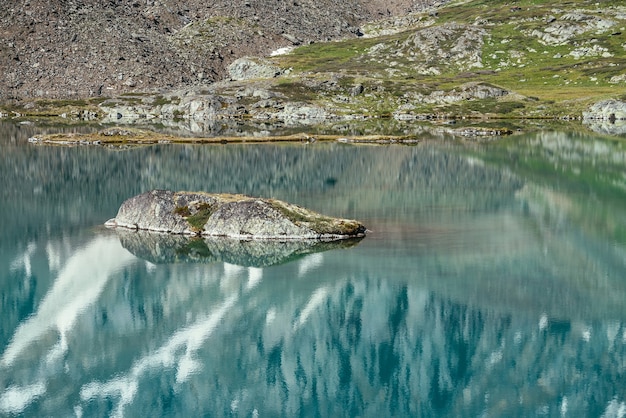 Felsen im türkisfarbenen Bergsee. Schneebedeckter Berg spiegelt sich im azurblauen klaren Wasser des Gletschersees. Schöner sonniger Hintergrund mit schneeweißer Gletscherreflexion in der grünen Wasseroberfläche des Bergsees.