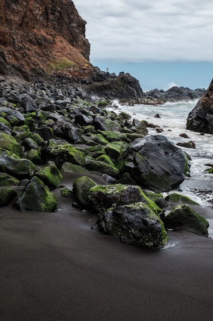 Felsen mit Moos und rauer See am Strand