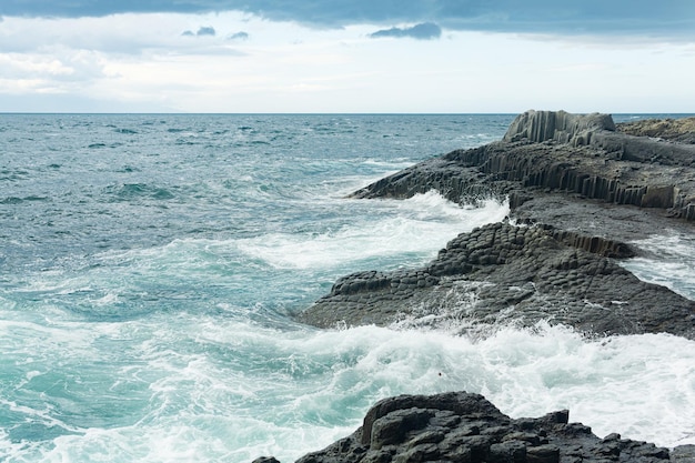 Felsige Küste aus säulenförmigem Basalt vor dem Hintergrund einer stürmischen Meeresküstenlandschaft der Kurilen