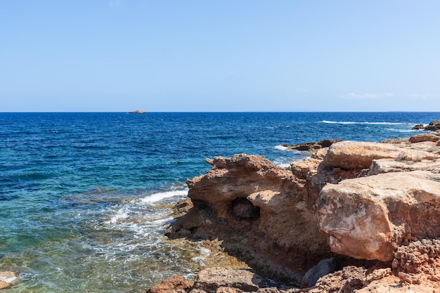 Felsige Küste in rosa Farben im Kontrast zum strahlend blauen Meer und hellblauen Himmel Ibiza
