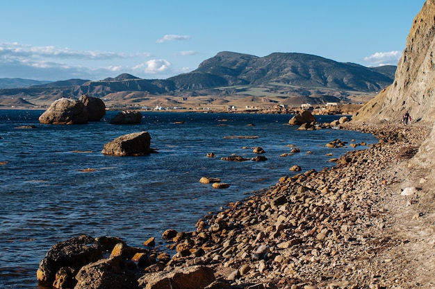 Felsiger Strand des Meeres vor dem Hintergrund des blauen Himmels und der Berge