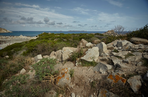 Felsiges und trockenes Gebiet mit mediterraner Vegetation, die typisch für die Südküste Sardiniens ist, mit dem Meer im Hintergrund.