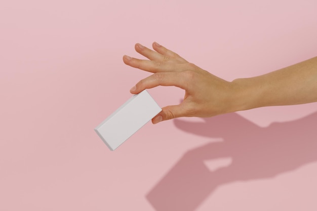 female hand holding white mockup box on pink isolated background concept for advertising and presentation of beauty confectionery or health product packaging and branding template for your design