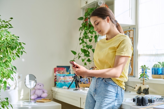 Fêmea adolescente usando smartphone descansando em casa no espaço da cópia do quarto