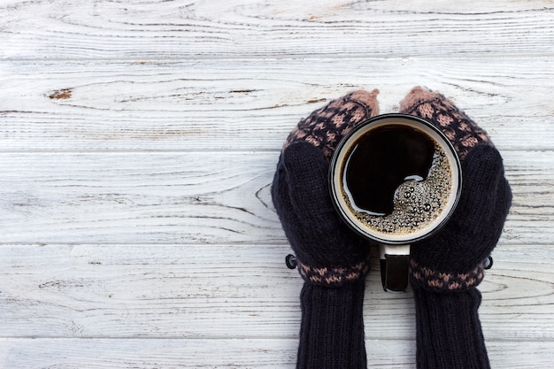 Fêmea as mãos em luvas segurando uma xícara de café sobre fundo de madeira