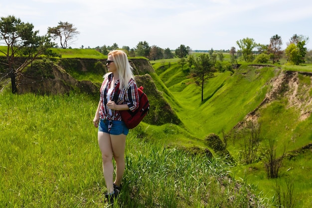 Fêmea aventureira feliz fica na encosta verde da montanha entre rododendros rosa floridos e olhando para a distância. Viagem épica nas montanhas. Ângulo amplo.