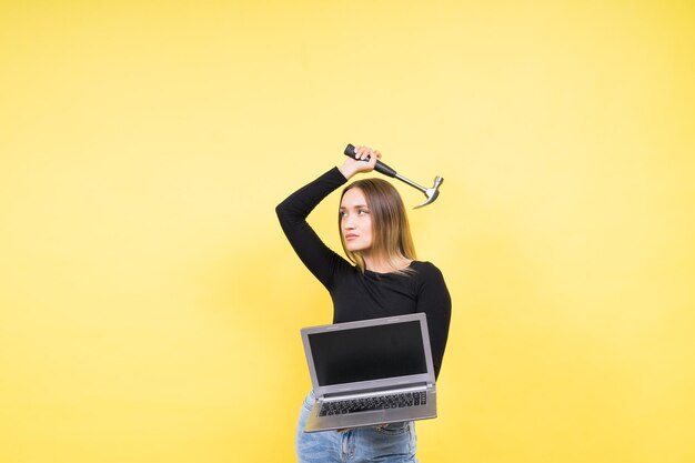 Fêmea de reparo de laptop com martelo e laptop em fundo amarelo