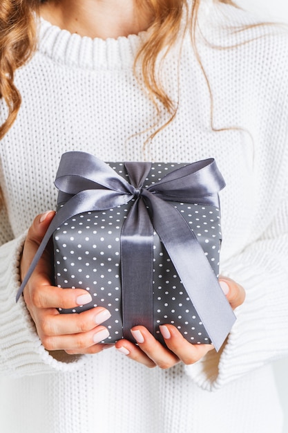 Fêmea de suéter branco de lã, segurando uma caixa de presente com um laço. Layout festivo de Natal. Maquete para o ano novo.