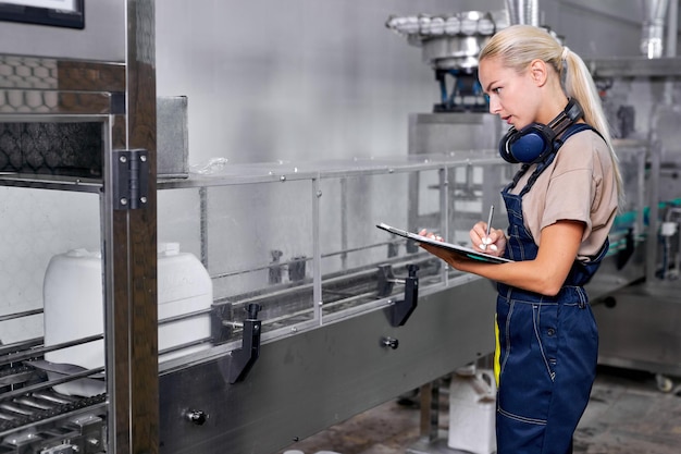 Fêmea de uniforme verificando e contando a quantidade e qualidade das latas de agrotóxicos e agroquímicos, anotar em folder-tablet. mulher de roupa azul está envolvida no trabalho, concentrada