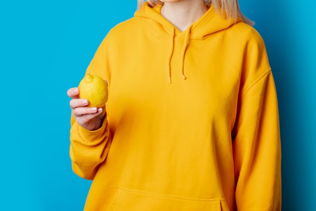 Foto fêmea elegante com capuz amarelo com limão sobre fundo azul