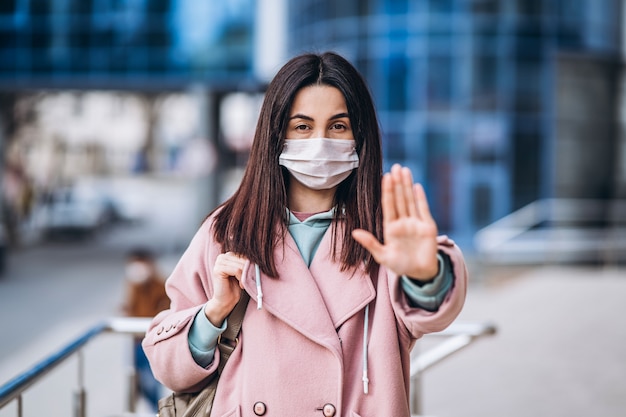 Fêmea em máscara médica ao ar livre mostra sinal de parada por suas mãos para distância social segura para evitar a infecção pelo vírus. Conceito de coronavírus, COVID-19, vírus, doença, epidemia, pandemia e quarentena.