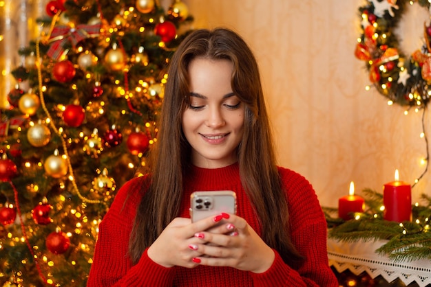 Fêmea feliz usando telefone celular na sala de estar decorada para o Natal