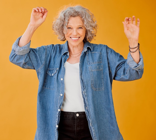 Fêmea madura e divertida na moda celebra a liberdade contra o fundo laranja feliz e despreocupada Mulher sênior positiva faz dança da vitória animada para a aposentadoria Senhora de espírito livre hippie se divertindo