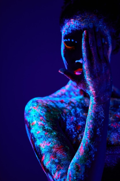 Foto fêmea negra hipnotizante com impressões fluorescentes na pintura cósmica da pele brilhando em luzes de néon