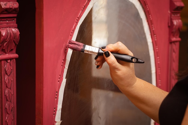 Fêmea noiva com pincel nas mãos pintando enfeites artesanais da velha porta do armário de madeira na cor rosa dando nova vida às coisas antigas restauração manual de móveis antigos