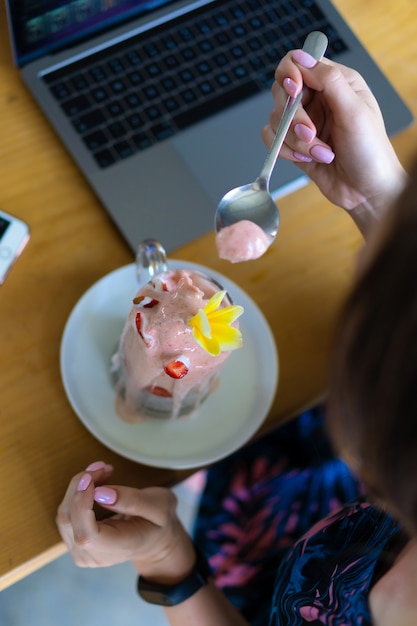 Fêmea nova que trabalha em um portátil, café da manhã saudável com sementes e suco do chia.