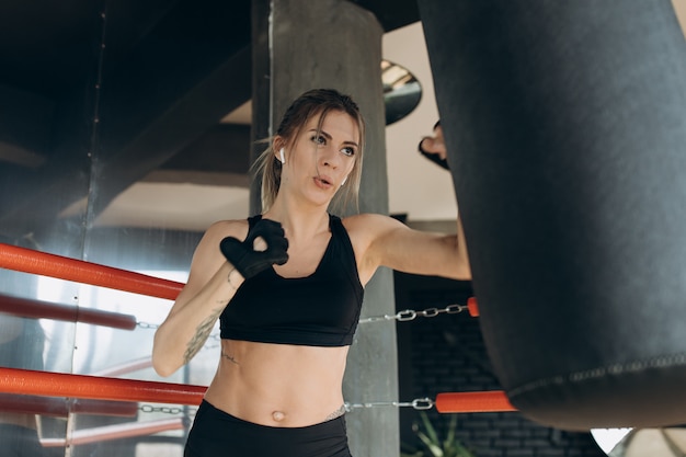 Fêmea, perfurando um saco de boxe com luvas de boxe no ginásio