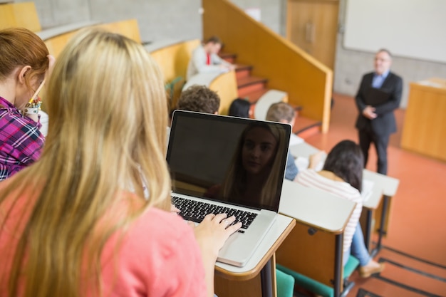 Foto fêmea que usa o laptop com alunos e professor na sala de aula