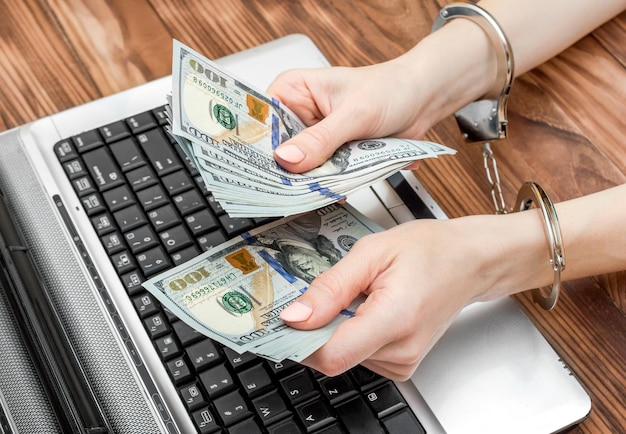 Fêmea segurando dinheiro nas mãos que estão trancadas por algemas sobre laptop