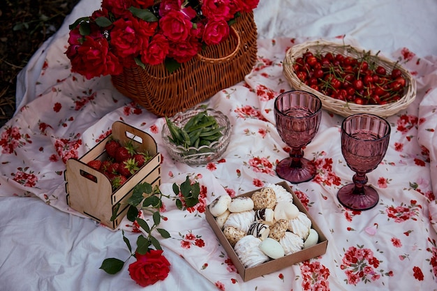 Feminin ästhetisches Sommerpicknick mit Tischdecke Marshmallows Erdbeergläser Wein zwischen rosa Rosen im Park Romantische Abendreise und Wertschätzung des Augenblicks