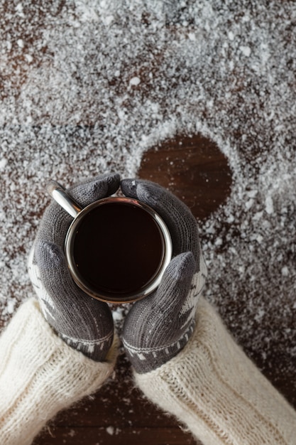 Femininas mãos segurando um café quente acima da mesa de madeira. Vista superior com espaço de cópia