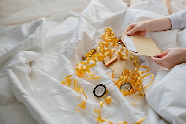 Femininas mãos segurando um cartão de presente, envelope e caixa de presente sobre o cobertor da cama. ano novo e o conceito de natal. vista horizontal superior