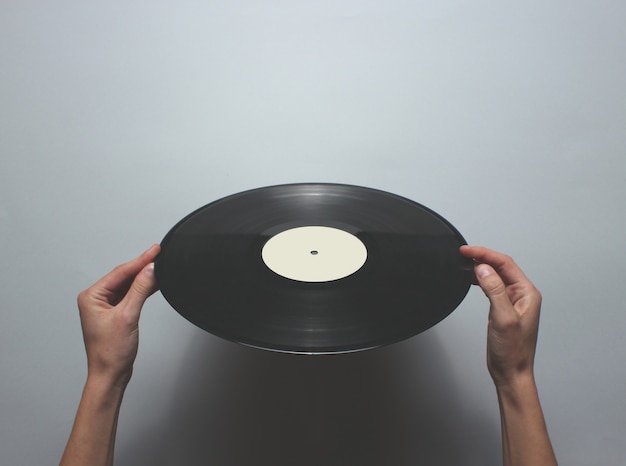 Femininas mãos segurando um disco de vinil retrô sobre uma mesa cinza. Vista superior, minimalismo.