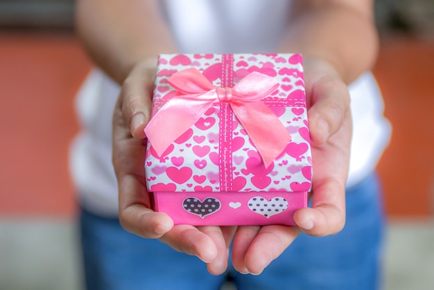 Femininas mãos segurando um pequeno presente com fita.