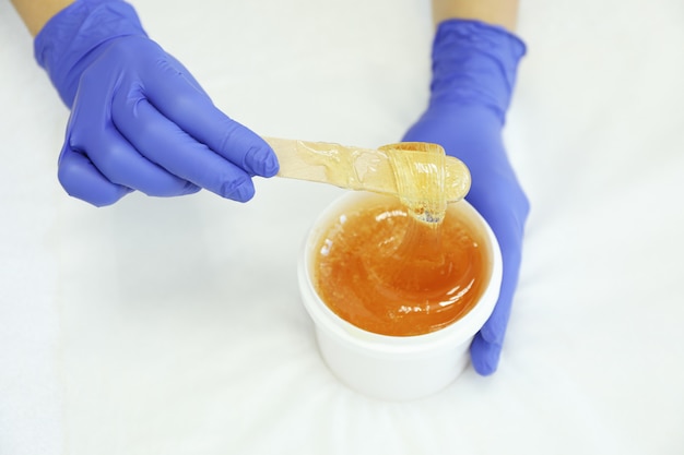 Femininas mãos segurando uma pasta amarela líquida para shugaring em branco, copie o espaço