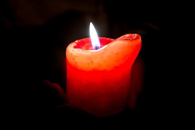 Femininas mãos segurando uma vela acesa na escuridão, abraçando-o