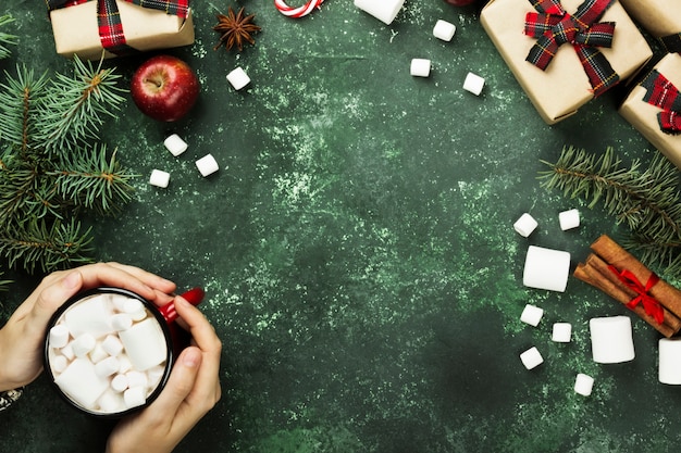 Femininas mãos segurando xícara com chocolate quente e vários atributos de férias em cinza, vista superior, copie o espaço