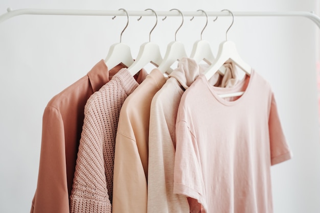 Feminine Kleidung in Pastellrosa Farbe auf Kleiderbügel auf weißem Hintergrund. Frühjahrsputz Hausgarderobe. Minimales Modekonzept.