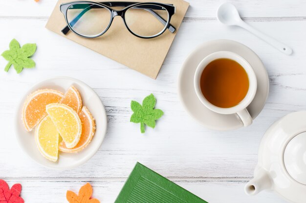 Feminine Schreibtischarbeitsfläche flach lag mit Tagebuch, Brille, Buch, Teetasse, Süßigkeiten und Filzdekor.