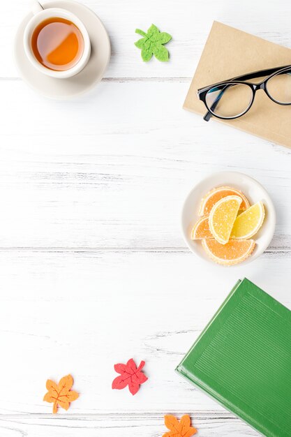 Feminine Schreibtischarbeitsfläche flach lag mit Tagebuch, Brille, Buch, Teetasse, Süßigkeiten und Filzdekor.