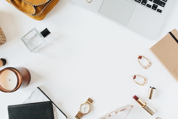 Femininer moderner Home-Office-Schreibtischarbeitsplatz mit Laptop, Parfüm, Uhr, Lippenstift, Pinsel und Zubehör auf weißer Oberfläche