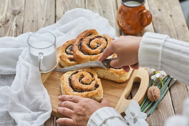 Feminino mão cortar pães caseiros com geléia, servido na mesa de madeira velha com nozes e copo de leite