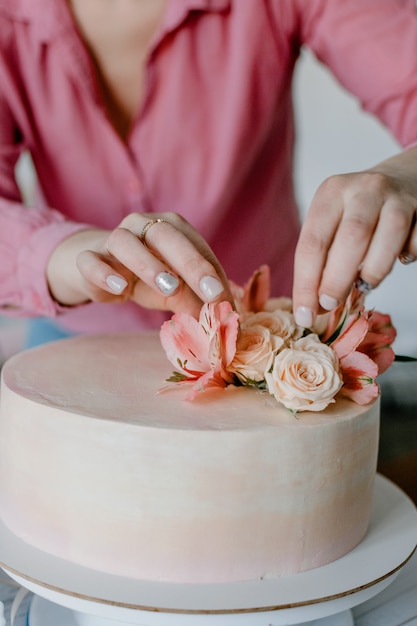 Feminino mão decorando o bolo de aniversário de casamento flor rosa no carrinho.