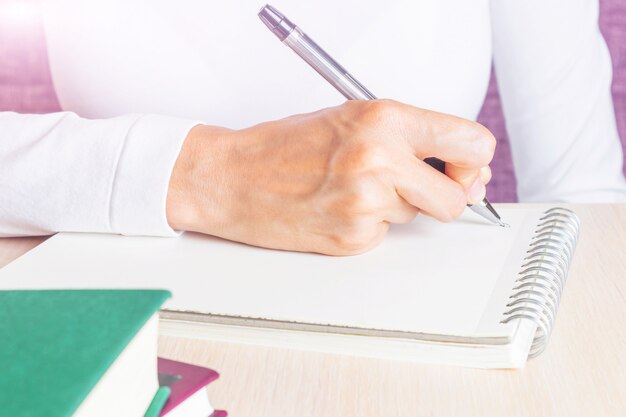 Feminino mão escreve no caderno por caneta.