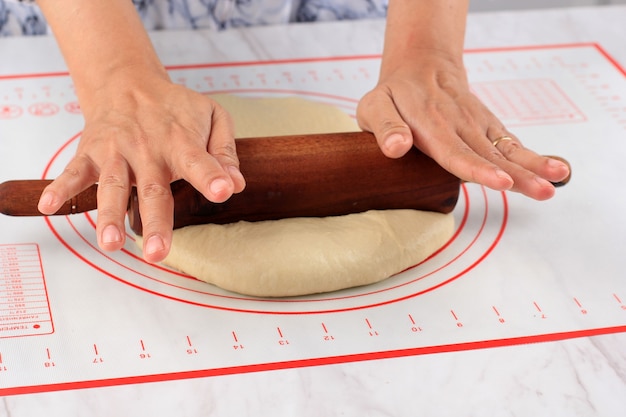 Feminino mão rolada pizza ou massa de pão com um rolo sobre uma mesa branca, polvilhada com farinha. cozinhar passo a passo na cozinha