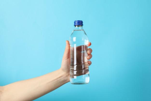 Feminino mão segura a garrafa com água em azul, close-up