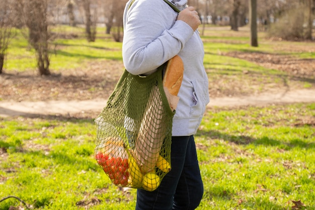 Feminino mão segura um saco de malha de algodão ecológico verde com um monte de frutas orgânicas, legumes e compras
